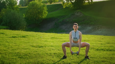 A-woman-squats-with-dumbbells-in-the-park-at-sunset-while-performing-exercises-wooded-thigh-muscles